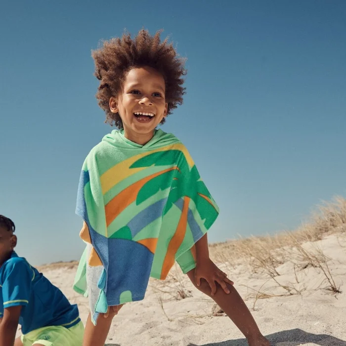 Little boy wearing a hooded beach towel with palm print colourful pattern