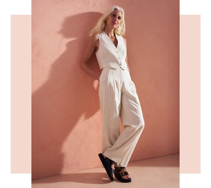 Woman wearing a cream pinstripe co ord with wide leg trouser and a waistcoat with black sandals