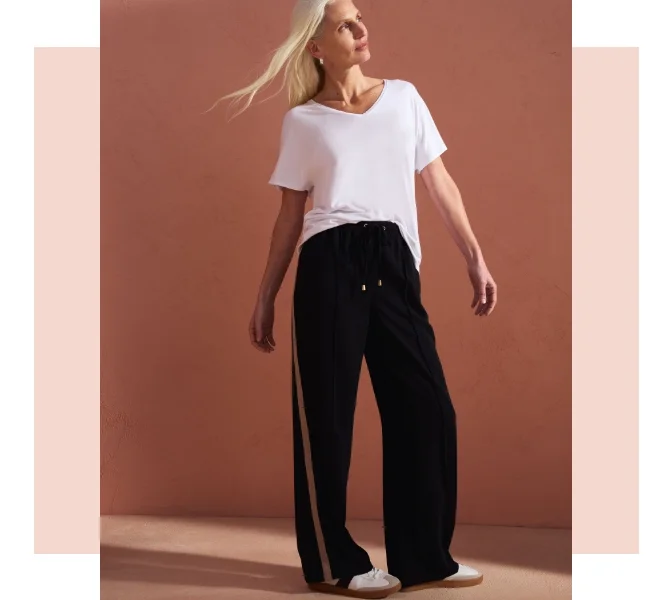 Woman wearing wide leg navy joggers with a stripe down the leg with a baggy white t shirt and white trainers