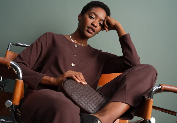 Woman with clutch bag and statement necklace sitting on chair.