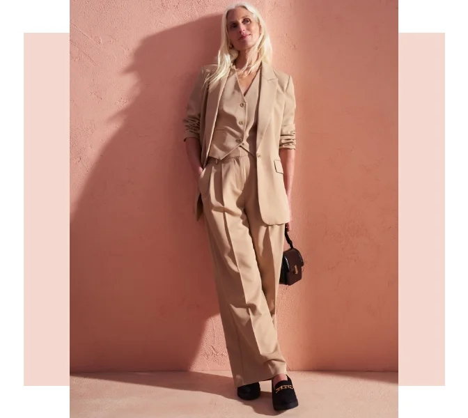 Woman wearing a full beige suit with wide leg trouser and a chunky black loafers and a black handbag