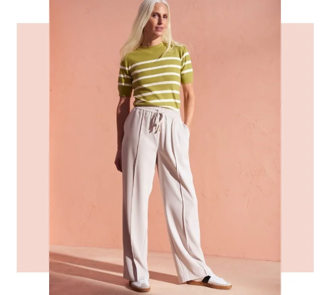 Woman wearing white wide leg joggers with a striped top and trainers