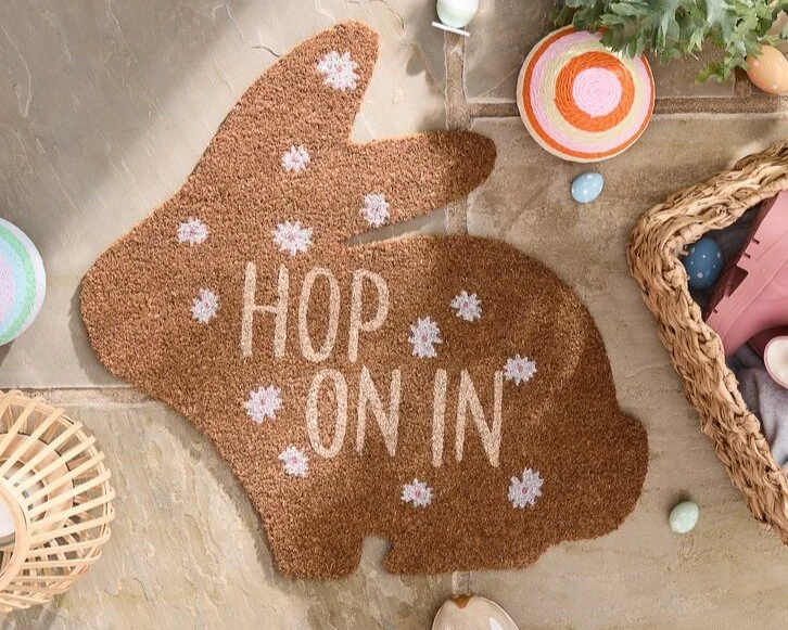 Easter doormat that is bunny shaped with the words 'hop on in' on it.